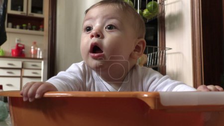 Adorable small baby toddler inside large plastic laundry bucket at kitchen