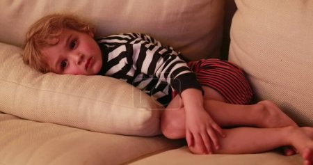 Photo for Candid child watching TV screen while laid in living-room sofa - Royalty Free Image