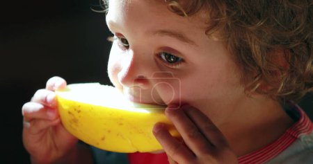 Photo for Small boy eating melon fruit for breakfast, toddler takes a bite of fruit and wiping mouth with arm - Royalty Free Image