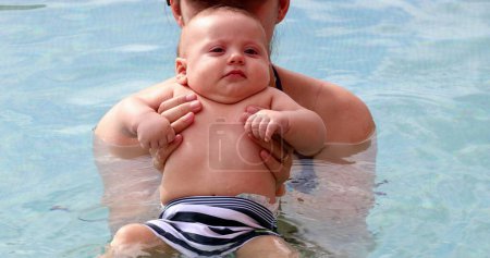 Foto de Mother holding newborn baby inside swimming pool water - Imagen libre de derechos