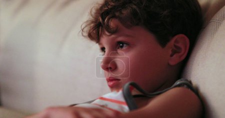 Photo for Child watching TV screen, casual candid young boy seated at living-room sofa - Royalty Free Image