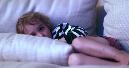 Photo for Child watching TV screen while laid in living-room sofa - Royalty Free Image