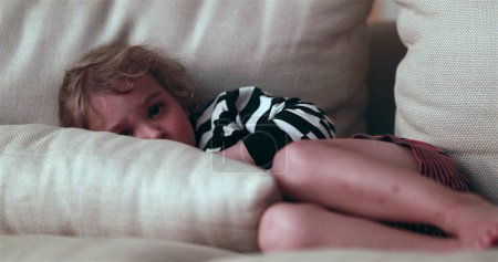 Téléchargez les photos : Child watching TV screen while laid in living-room sofa - en image libre de droit