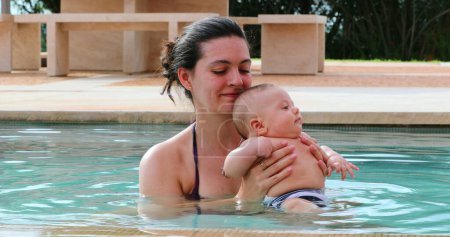 Foto de Mother holding newborn baby inside swimming pool water - Imagen libre de derechos