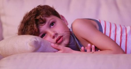 Photo for Tired child young boy gradually falling asleep in living room sofa in the evening watching movie - Royalty Free Image