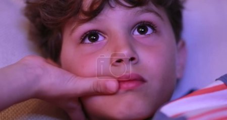 Photo for Young boy staring TV screen at night, real life candid child watching content - Royalty Free Image