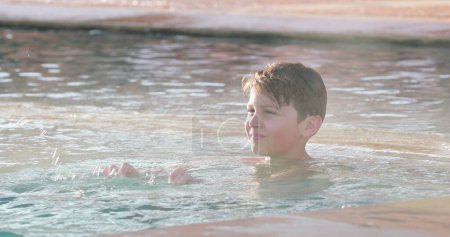 Photo for Small boy inside warm heated jacuzzi pool with water steaming - Royalty Free Image