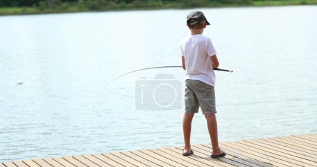 Téléchargez les photos : Young boy fishing by a lake river standing by pier - en image libre de droit