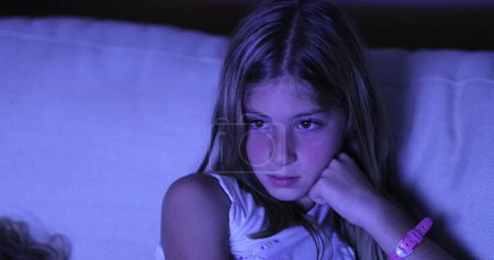 Téléchargez les photos : Candid enfant fille regarder écran de télévision dans le noir, Petite fille regardant un film - en image libre de droit