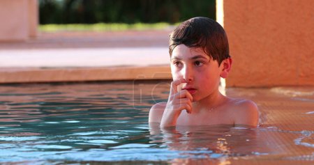 Photo for Candid thoughtful young boy at the swimming pool thinking lost in thought in contemplation - Royalty Free Image