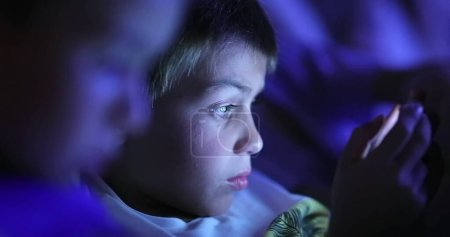 Téléchargez les photos : Enfants devant l'écran de la tablette avec une lumière bleue qui brille dans le visage - en image libre de droit