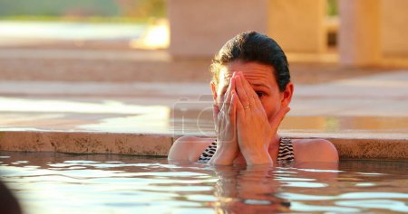 Téléchargez les photos : Femme franche réfléchie à la piscine affligeante couvrant le visage pensant à l'intérieur de l'eau - en image libre de droit