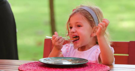 Téléchargez les photos : Candid jolie petite fille manger dessert sucré avec cuillère - en image libre de droit