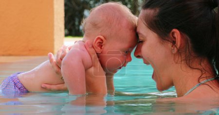 Foto de Mother and baby infant at the pool together interaction. Mom kissing and hugging baby son, showing love and affection - Imagen libre de derechos
