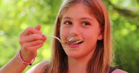 Photo for Little girl eating sweet with spoon. Child eats dulce de leche snack. Portrait of girl eating dessert - Royalty Free Image