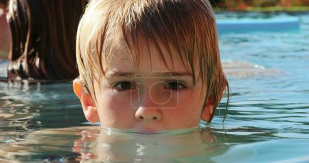 Téléchargez les photos : Petit garçon regardant à la caméra portrait à l'eau de la piscine - en image libre de droit