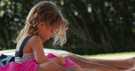Téléchargez les photos : Enfant petite fille regardant l'appareil smartphone à l'extérieur - en image libre de droit