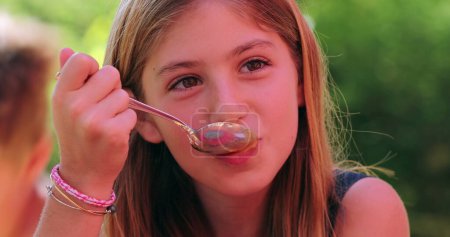 Photo for Happy little girl eating dessert with spoon looking to camera smiling and laughing. Child eating dulce de leche - Royalty Free Image