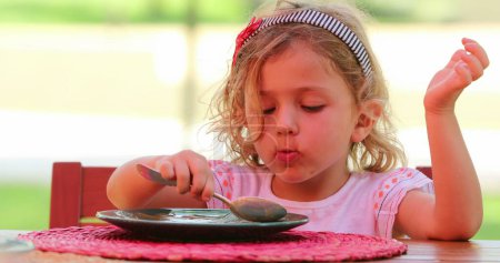 Photo for Child eating dessert sweet with spoon, small girl blond eating snack outdoors - Royalty Free Image