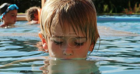 Téléchargez les photos : Petit garçon à l'intérieur de l'eau de la piscine regardant à la caméra pensée portrait - en image libre de droit