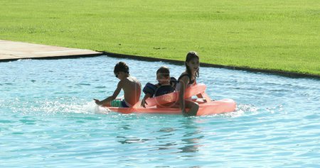Children playing the swimming pool water on top of inflatable mattress