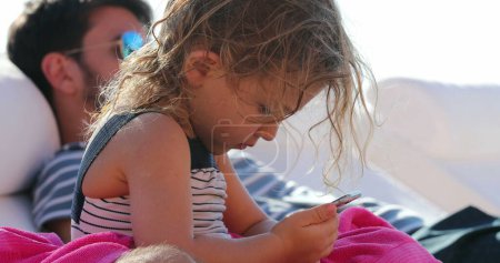Téléchargez les photos : Petite fille tenant et regardant l'appareil smartphone à l'extérieur - en image libre de droit