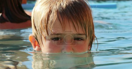 Téléchargez les photos : Portrat de petit garçon enfant à l'intérieur de l'eau de la piscine regardant à la caméra - en image libre de droit