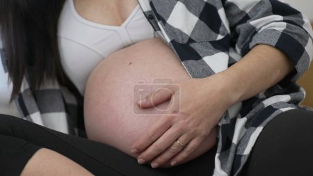 Foto de Embarazo en fase tardía: mujer acariciando el primer plano del vientre, comodidad del tercer trimestre - Imagen libre de derechos