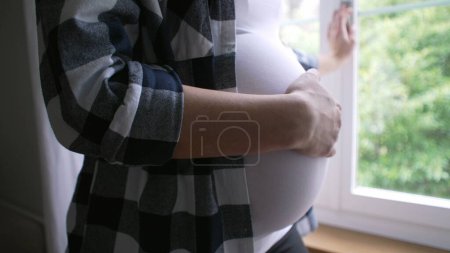 Foto de Primer plano de la madre acariciando el vientre, esperando un hijo recién nacido - embarazo de 8 meses por ventana de residencia - Imagen libre de derechos