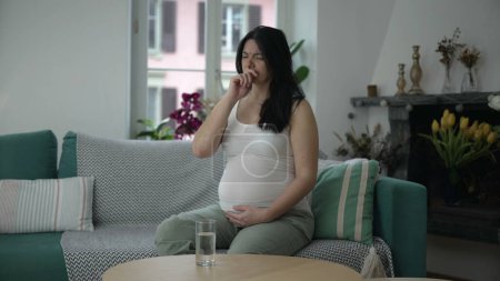 Foto de Mujer embarazada que experimenta molestias, señora de 30 años con náuseas del tercer trimestre sentada en el sofá del hogar - Imagen libre de derechos