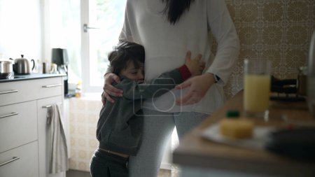 Téléchargez les photos : Affectueux Embrassez-vous dans la cuisine - Jeune garçon cherchant câlin de la mère, Interaction familiale réconfortante capturée dans un cadre familial authentique - en image libre de droit