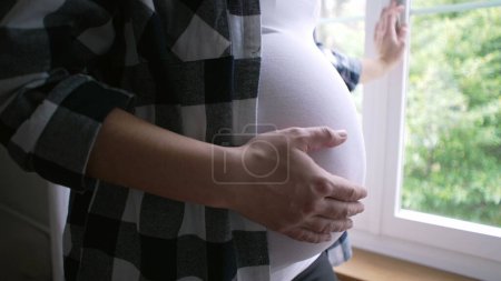 Foto de Primer plano de la madre acariciando el vientre, esperando un hijo recién nacido - embarazo de 8 meses por ventana de residencia - Imagen libre de derechos
