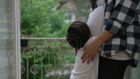 Little Boy Expressing Love by Kissing Mother's Pregnant Belly, Tender Third Trimester Moment on Home Balcony, brother hugging unborn baby