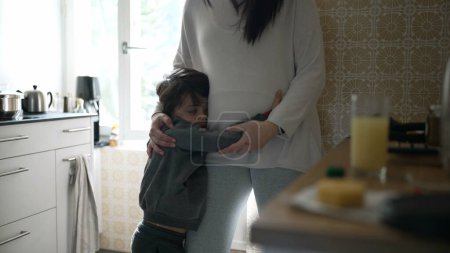 Foto de Abrazo cariñoso en la cocina - Joven buscando un abrazo de mamá, conmovedora interacción familiar capturada en un entorno casero auténtico - Imagen libre de derechos