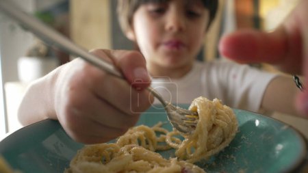 Child eating spaghetti noddles furing mealtime, close-up face of 5 year old little boy enjoying carb rich food