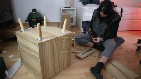 Muebles que ensamblan de la mujer en el nuevo hogar, usando la máquina de perforación para la construcción de la mesita de noche, incorporando la autosuficiencia en la mejora casera
