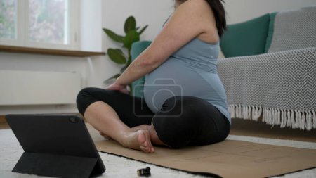 Téléchargez les photos : 30s future mère sur tapis de yoga engagé dans le dos doux étirement pour les soins prénataux, se concentrant sur le corps et le bien-être dans la routine d'entraînement de salon - en image libre de droit