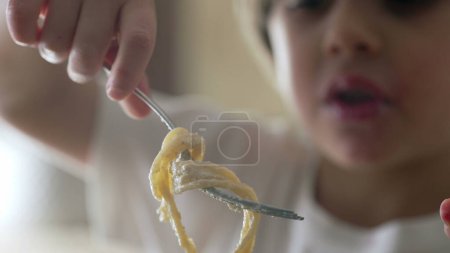 Child eating pasta - close-up of small boy holding fork attempts to spin spaghetti, learning to use fork while enjoying rich carb food