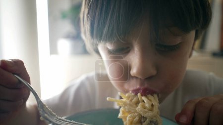 Child eating pasta, hungry 5 year old little boy eats carb food, kid enjoying cheese spaghetti, close-up face and food