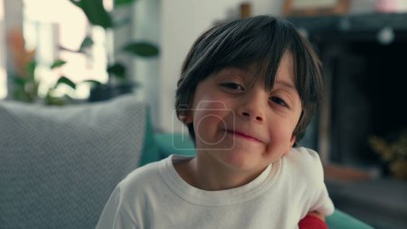 Téléchargez les photos : Gros plan Portrait d'un garçon de 5 ans assis sur un canapé, résidence intérieure, émotion heureuse - en image libre de droit