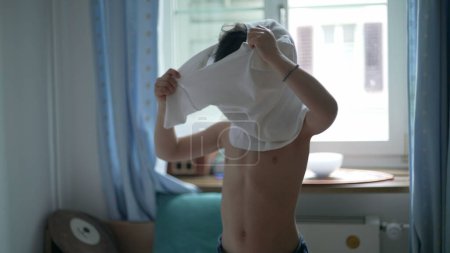 Foto de Niño poner camiseta, joven vestir por sí mismo de pie en la ropa del dormitorio camisa blanca. Niño caucásico de 5 años - Imagen libre de derechos