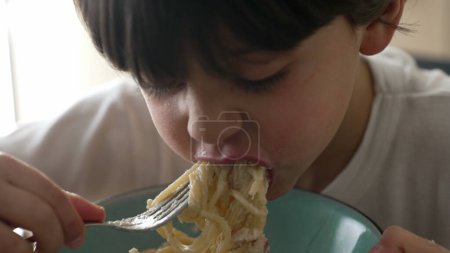 Téléchargez les photos : Pâtes alimentaires pour enfants, petit garçon de 5 ans affamé mange de la nourriture carb, enfant dégustant des spaghettis au fromage, gros plan sur le visage et de la nourriture - en image libre de droit