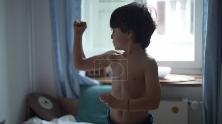 Photo for Adorable little boy showing his muscles, happy 5 year old male caucasian child flexing arms in bedroom - Royalty Free Image