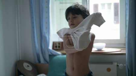 Enfant mettant t-shirt, jeune garçon habiller par lui-même debout dans les vêtements de chambre à coucher chemise blanche. 5 ans caucasien mâle enfant