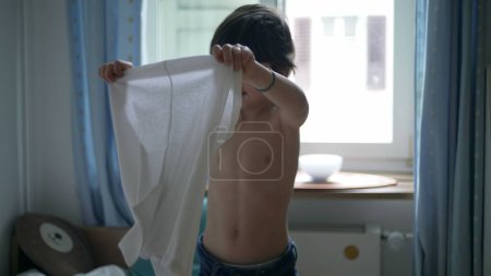 Enfant mettant t-shirt, jeune garçon habiller par lui-même debout dans les vêtements de chambre à coucher chemise blanche. 5 ans caucasien mâle enfant