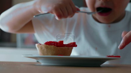 Foto de Niño luchando por alcanzar la tarta de queso con tenedor - Vista de cerca de la golosina azucarada rematada con fresas en la placa - Imagen libre de derechos