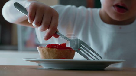 Téléchargez les photos : Lutte de l'enfant pour atteindre Cheesecake à la fourchette - Gros plan sur les friandises sucrées garnies de fraises sur une assiette - en image libre de droit