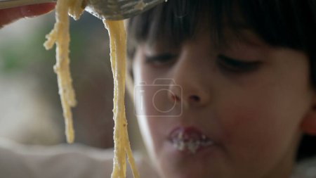 Pâtes alimentaires pour enfants - gros plan d'un petit garçon tenant une fourchette tente de faire tourner les spaghettis, apprenant à utiliser une fourchette tout en dégustant de la nourriture riche en glucides