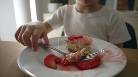Petit garçon mangeant du gâteau au fromage à la fraise sur une assiette en gros plan. Un enfant de 5 ans prend une bouchée de dessert sucré après le repas
