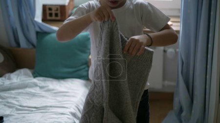 Photo for Little boy putting pullover standing in bedroom. 5 year old caucasian male kid dressing by himself clothing warm clothes during cold season - Royalty Free Image